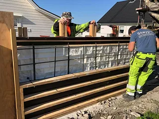 To håndverkere monterer forskaling og armering til dekorativ betongmur ved bolig.
