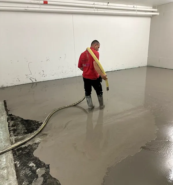 Arbeider sprer flytende betong med slange på gulvflate